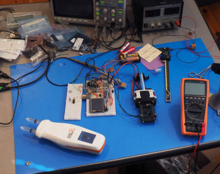 A breadboard next to a prototype syringe pump.